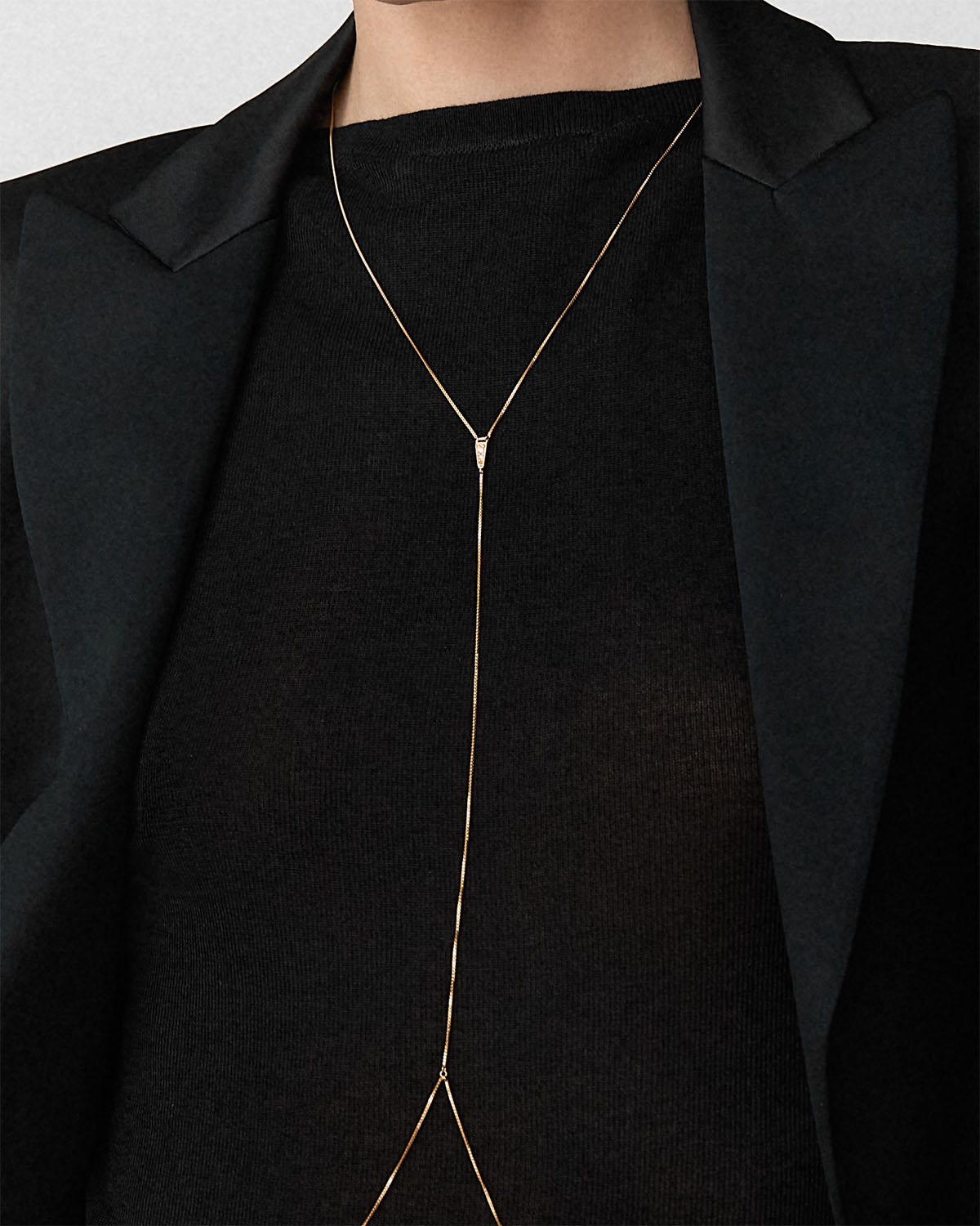 Close view of Bliss Lau Blink body chain worn by a model in a black knit top and black blazer.