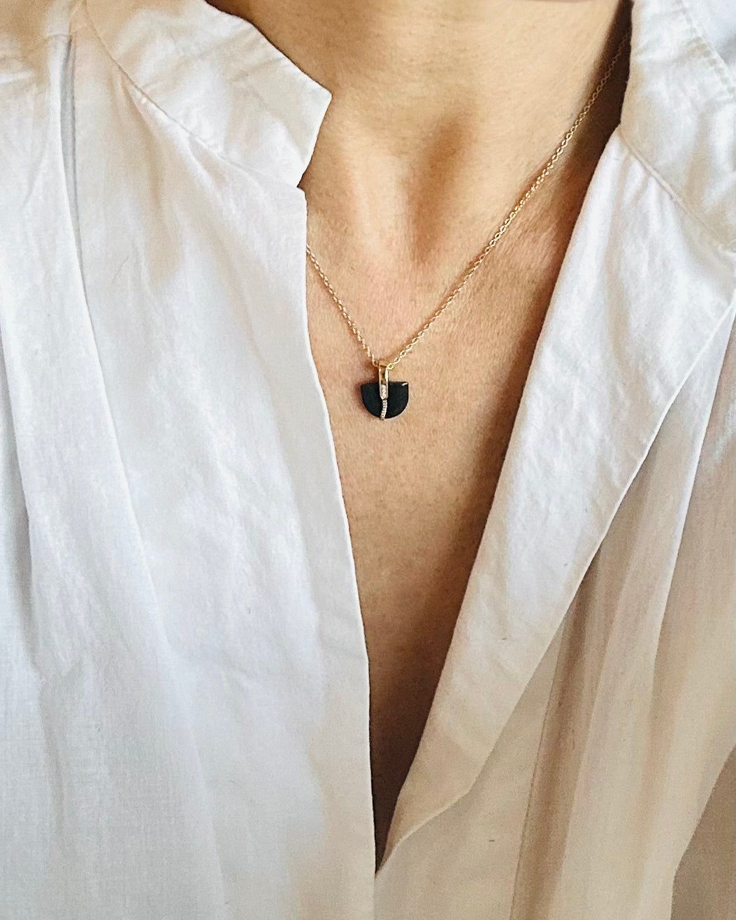 Gold Necklace with a half circle-shaped  black jade pendant worn under a white shirt