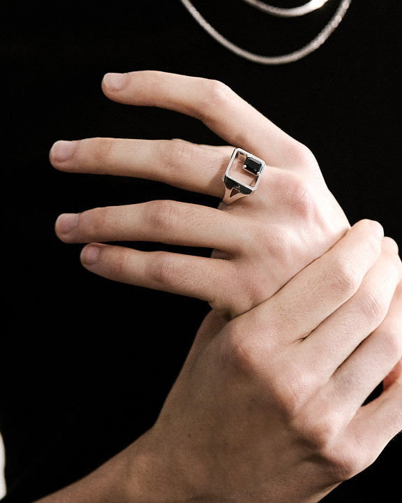 Close-up of a hand wearing a silver signet ring with a black spinel on a black background