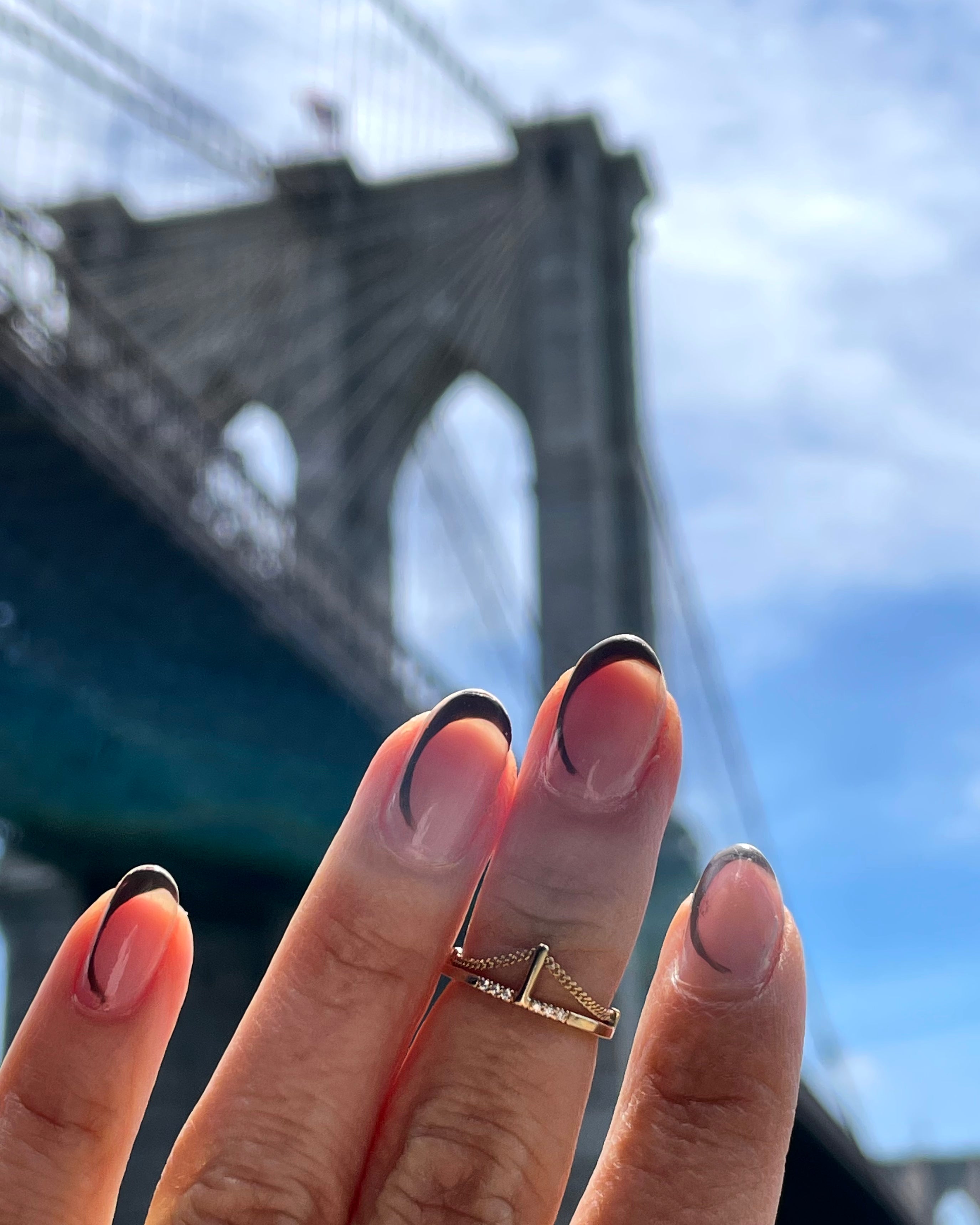 Hand with gold ring and chain in front of a brooklyn bridge