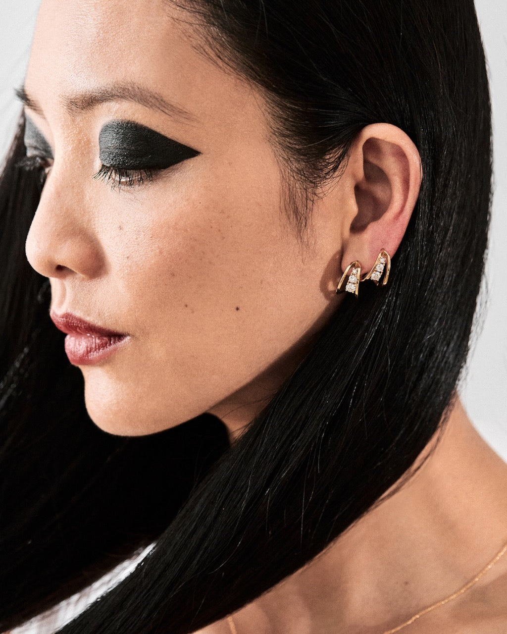 Close-up of a woman's ear with gold earrings with diamonds against a neutral background