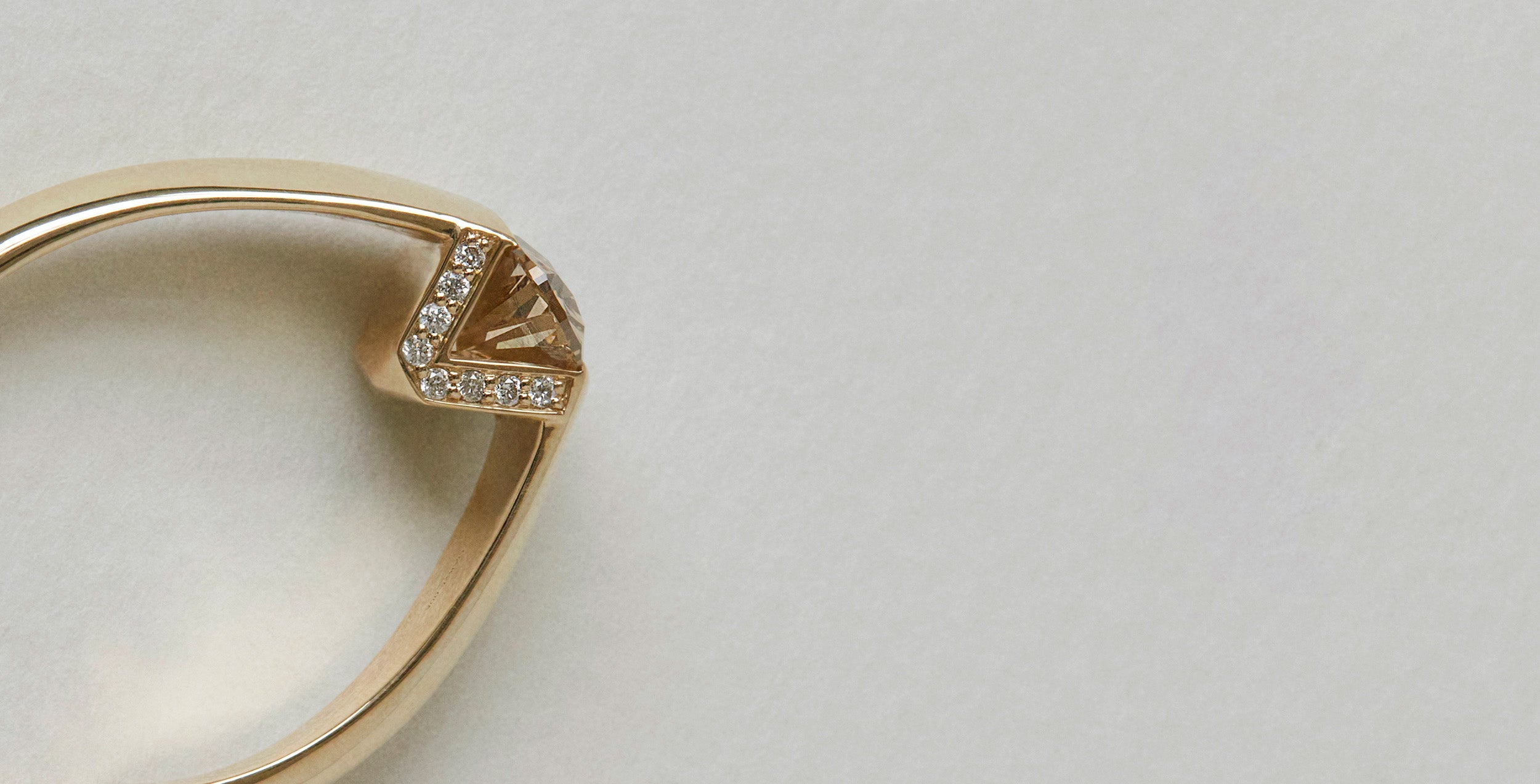 Bliss Lau Futurist Arc 14k Gold engagement ring with champagne diamond and small diamonds on a light gray background