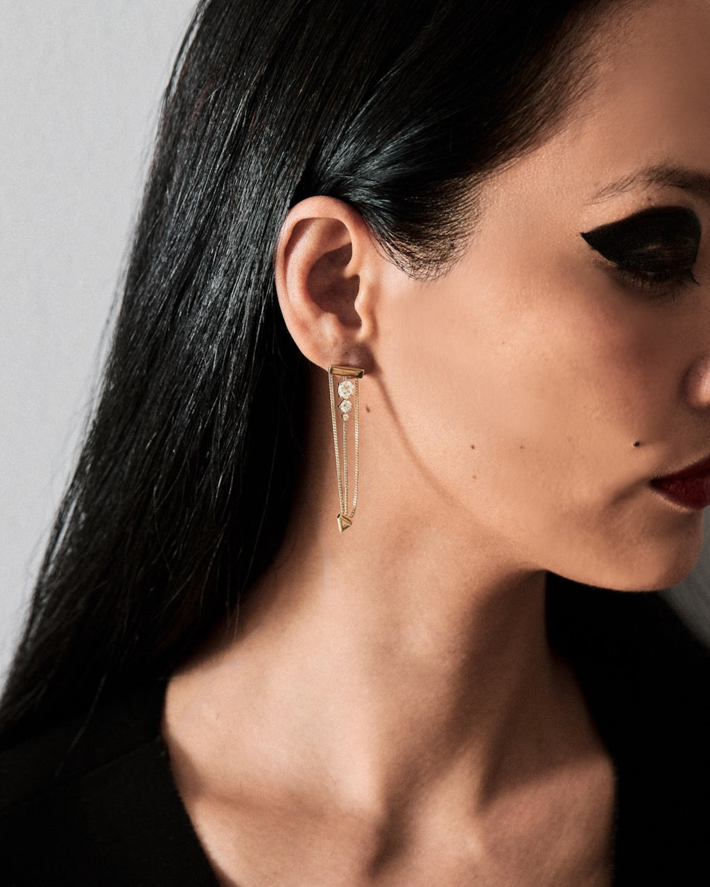 Close-up of a woman wearing a three diamond earring with gold chains against a neutral background