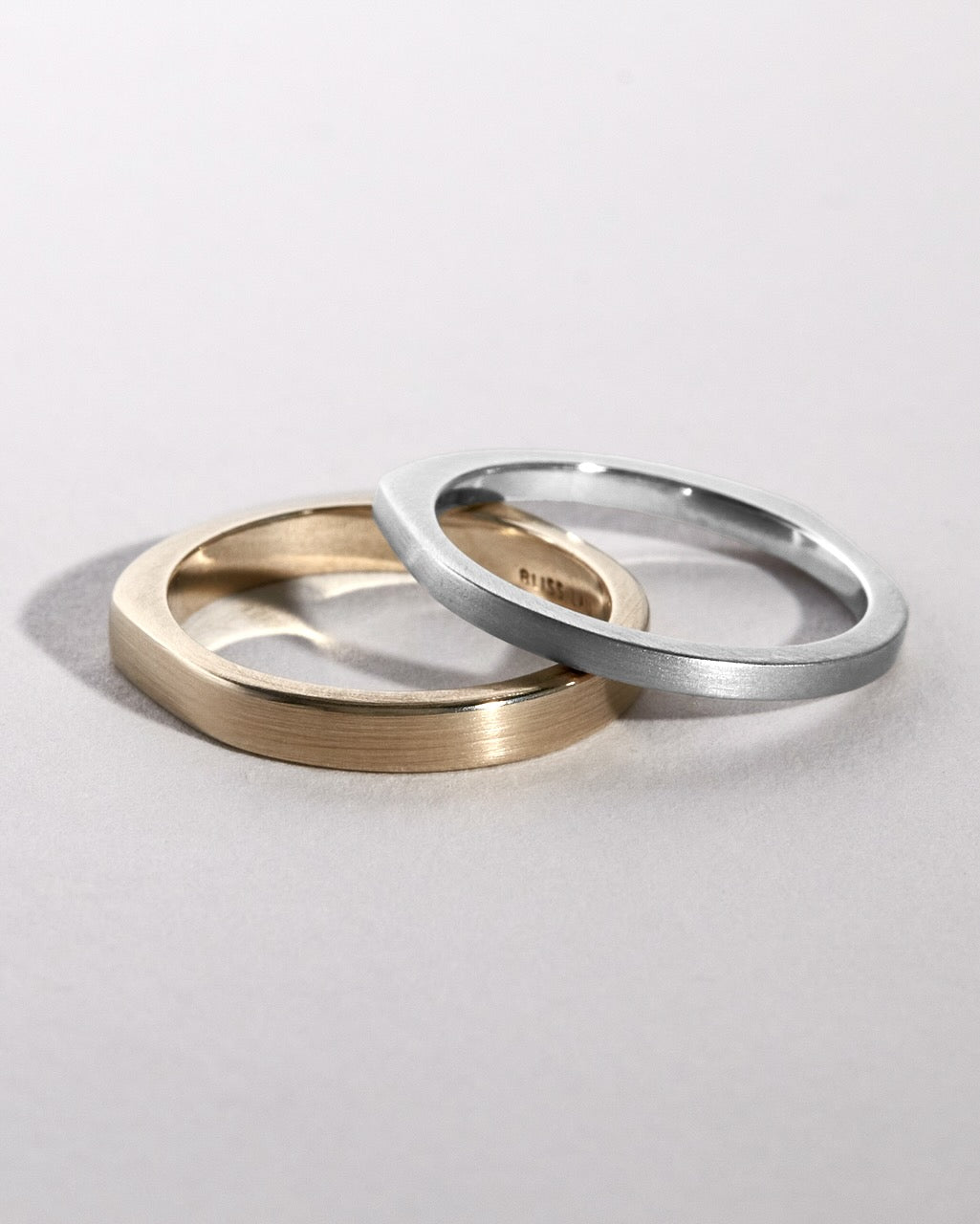 Two wedding rings, one gold and one platinum, on a light gray background