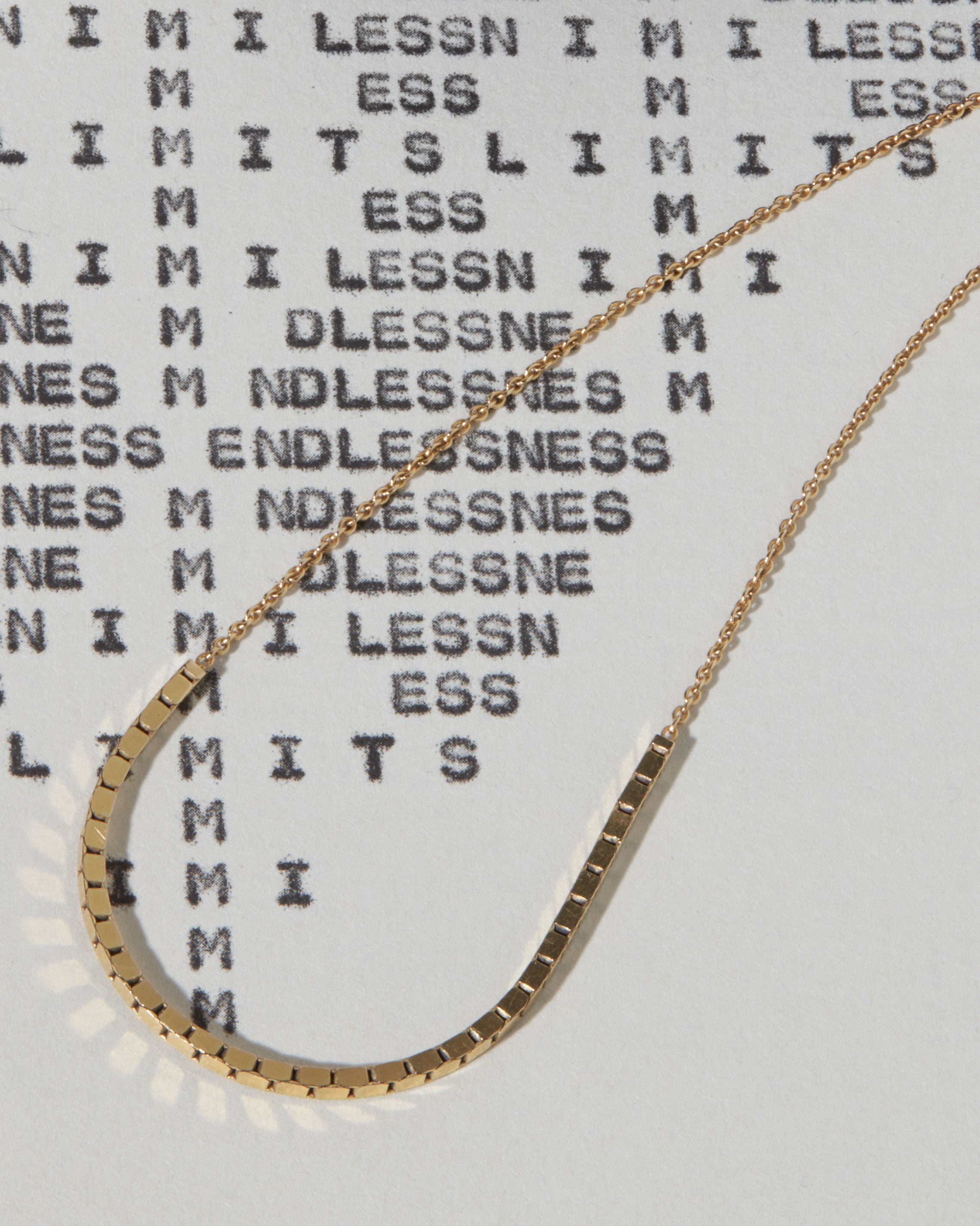 Halo Necklace artfully arranged over a textured backdrop, emphasizing its modern half-circle shape crafted from solid 18k gold.